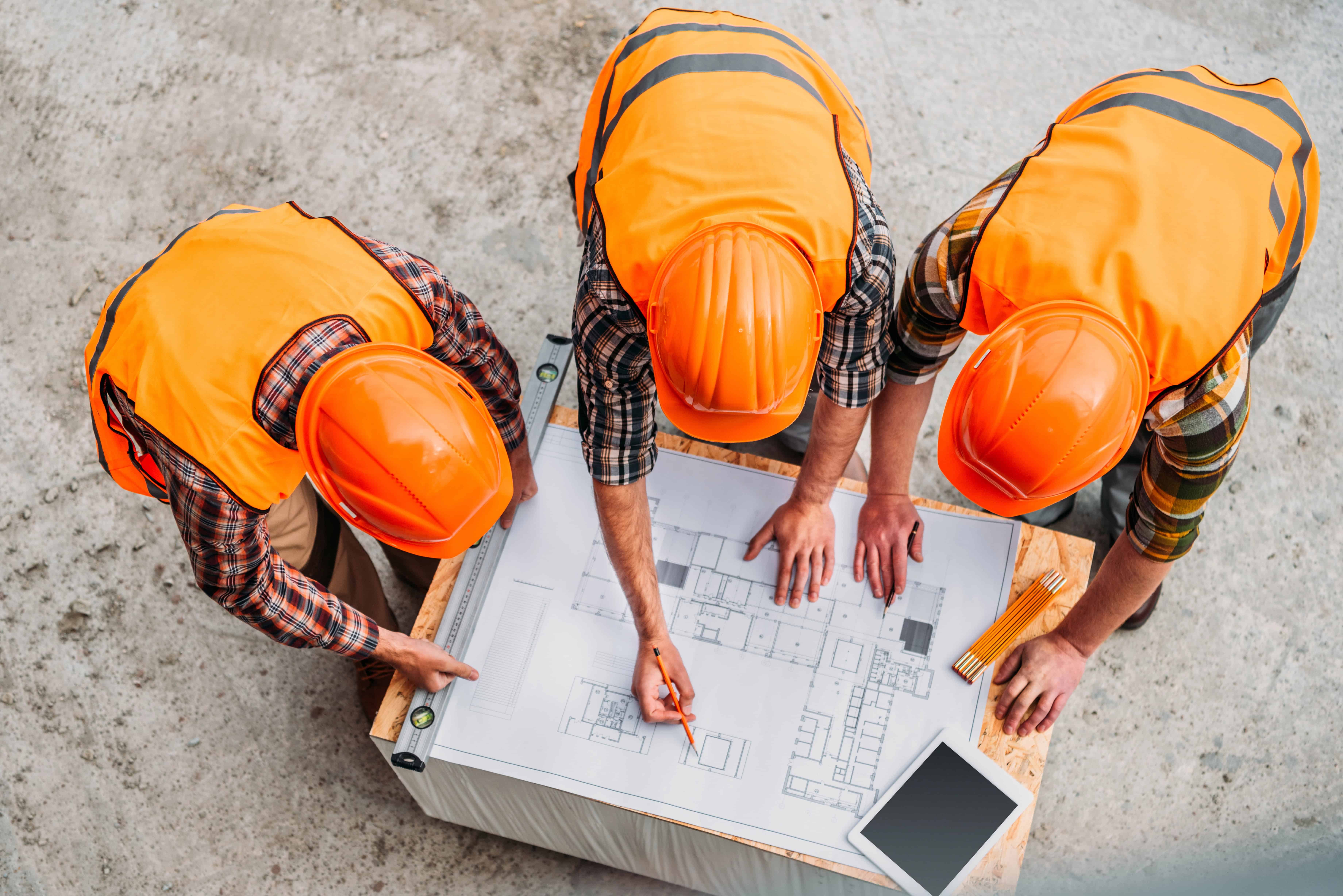 Industrial workers in hi-vis and hard hats following a written procedure at a work site.